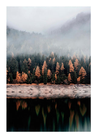 Autumn trees with orange foliage reflected on a calm lake, misty forest and mountains in the background.