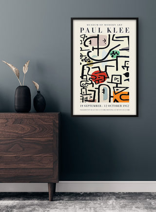 Framed Paul Klee exhibition poster with abstract art, displayed above a wooden dresser in a modern room.