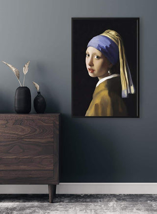 Framed "Girl With the Pearl Earring" poster by Johannes Vermeer on a gray wall above a wooden dresser.