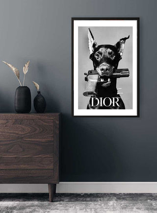 Framed Dior Dog Plakat featuring a black dog holding a purse, displayed on a dark gray wall above a dresser.