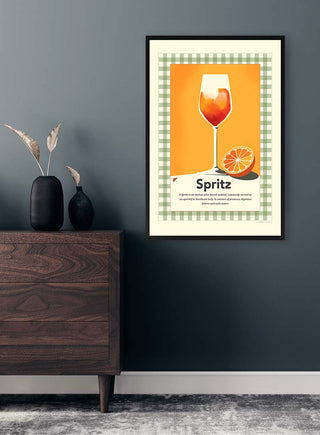 Framed Spritz retro print featuring a vibrant cocktail and orange slice, displayed on a modern dark wall above a dresser.