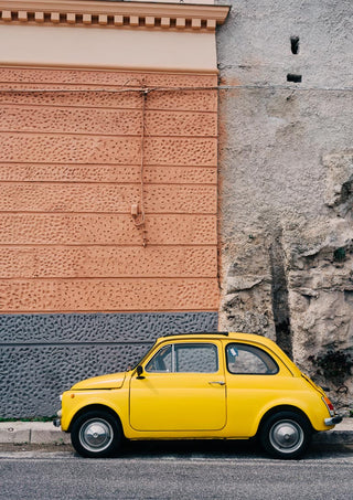 A yellow vintage car parked beside a textured wall on the Amalfi Coast Drive XII.