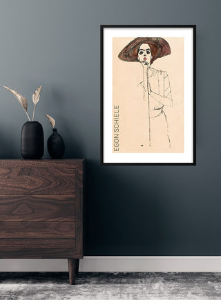 Framed "Portrait of a Woman" by Egon Schiele poster on a gray wall above a wooden dresser.