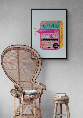 Framed Sardines Tin Can - Baroo Bloom artwork displayed above a wicker chair and small table with books.