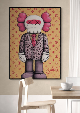 Framed SuitClub Kaws artwork by Danii Steinfeldt displayed on a beige wall above a table and chair.