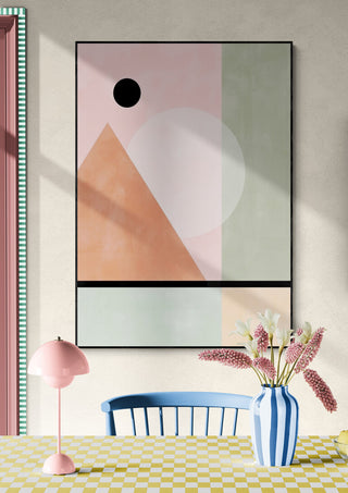 Framed artwork with pastel geometric shapes, including a triangle and circles, displayed above a table in a cozy room.