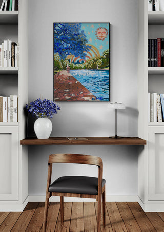 Framed "Rainbow" by Eleanor Baker hanging above a wooden desk with bookshelves, flowers, and a lamp.