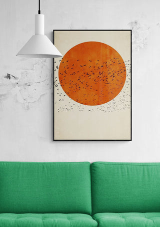 Framed "Birds In the Sun" by Boris Draschoff above a green couch, featuring birds and an orange sun.