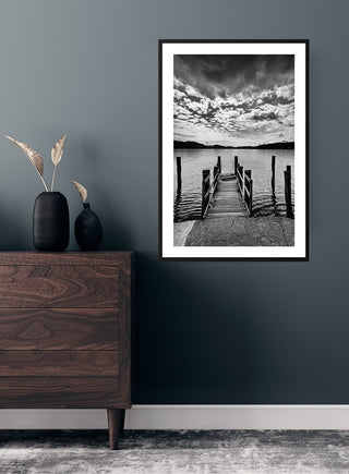Black and white poster of a wooden pier extending into a lake, displayed on a dark wall above a dresser.