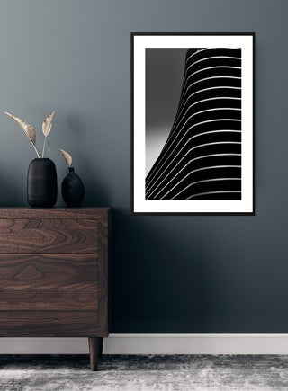 Framed poster of curved white lines on a black background, displayed above a dark wood dresser in a modern room.