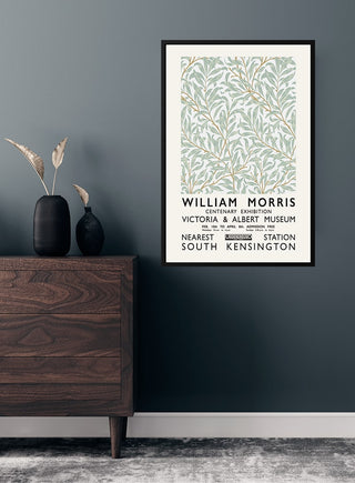 William Morris exhibition poster with botanical design, framed and hung on a dark wall above a wooden dresser.