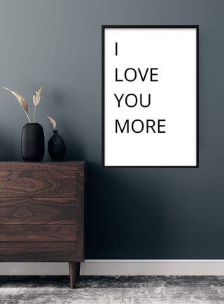 Framed "I LOVE YOU MORE" poster on a dark wall above a wooden dresser with decorative vases.