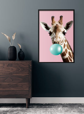 Poster of a giraffe blowing blue bubblegum on a pink background, displayed in a modern room.
