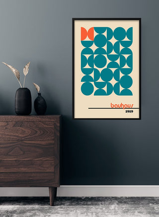 Bauhaus orange on blue poster with geometric shapes, framed and hung on a modern dark wall above a wooden dresser.
