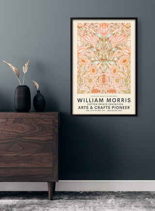 Framed William Morris Pink Exhibition Poster with floral design displayed on a dark wall above a wooden dresser.