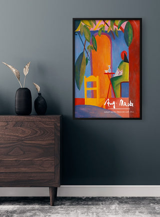 Framed August Macke - Türkisches Café Plakat poster on a dark wall above a wooden dresser in a modern room.