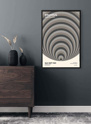 Bauhaus Big Circles Grey Plakat featuring concentric circles, framed on a dark wall above a wooden dresser.