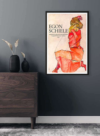 Framed Egon Schiele - Kniende in orange-rotem Kleid, 1910 poster on a dark wall above a wooden dresser.