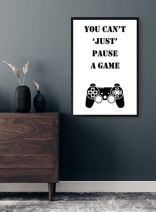 Framed "You Can't 'Just' Pause a Game" gamer poster with game controller, hanging above a dresser.