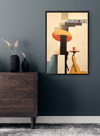 Framed Bauhaus Dress - David Wolf print on a dark wall above a wooden dresser with vases and dried plants.