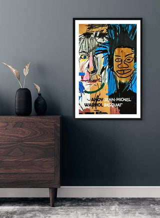 Framed Andy Warhol - Jean Michel Basquiat artwork displayed on a contemporary dark wall above a wooden dresser.