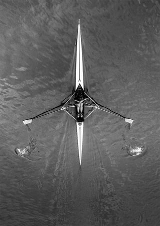 Overhead view of a single rower in a boat on the river, creating ripples in the water.