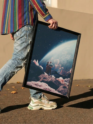Person holding a framed "Often Mistaken for Absent" art print by Frank Moth, showing a surreal space scene.