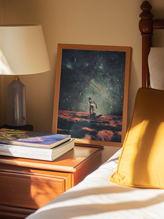 Nostalgia by Frank Moth art print leaning on a bedside table beside books and a lamp in a cozy bedroom.