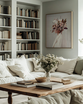 Framed "I Fell In Love With Fall Because of You" by Frank Moth above a cozy sofa with books and flowers.