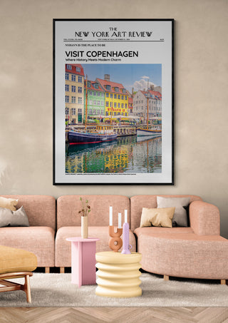 Framed Nyhavn - Art Review Plakat featuring colorful Copenhagen buildings, displayed above a modern pink sofa.