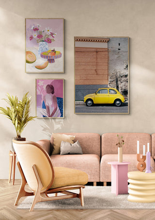 Framed print of a yellow car on the Amalfi Coast Drive XII displayed above a modern pink sofa in a stylish living room.