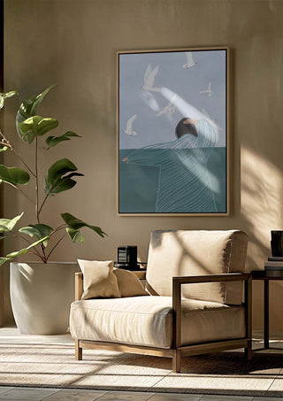Framed "Seaside" artwork by Bea Muller on wall above a beige armchair in a sunlit, modern living space.