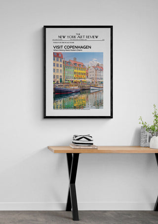 Framed Nyhavn - Art Review Plakat featuring colorful Copenhagen buildings, displayed above a wooden table.
