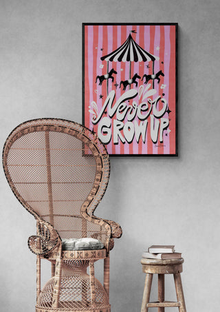 Framed Carousel - Never Grow Up art print with carousel horses on a pink background, displayed above a wicker chair.
