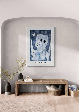 Framed "Angel Applicant 1939" by Paul Klee displayed on a light gray wall above a wooden bench.