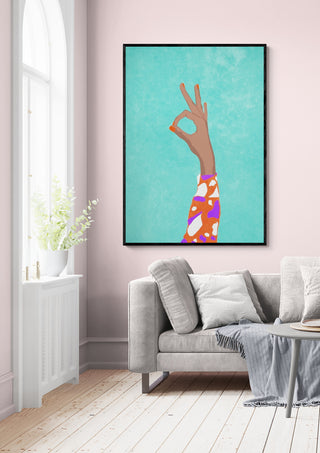 Framed "Okay" artwork by Raissa Oltmanns, featuring a hand making an OK gesture, displayed above a sofa.