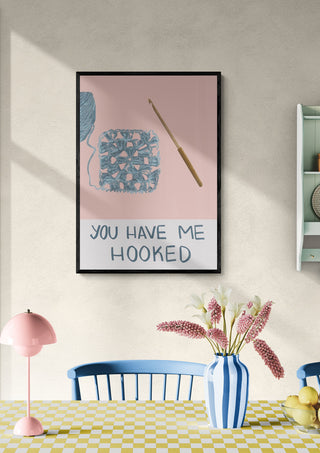 Framed crochet-themed wall art with yarn, hook, and "You have me hooked" on a dining room wall.