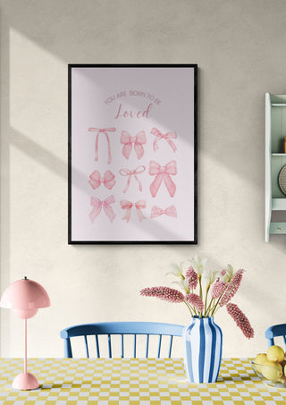 Framed print of pink bows with "You are born to be loved" text, displayed above a dining table.