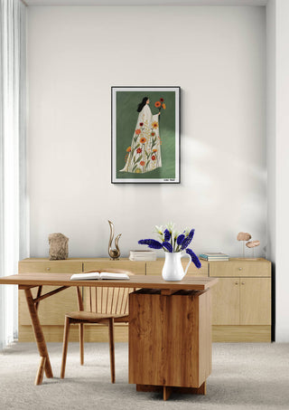 Blooming Grace by Elara Monet framed on a wall above a modern wooden desk with flowers and decor items.