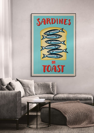 Framed "Sardines On Toast" wallchart displayed above a modern grey sofa in a stylish living room.