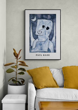 Framed print of Paul Klee's "Angel Applicant 1939" displayed above a white sofa with yellow pillows.