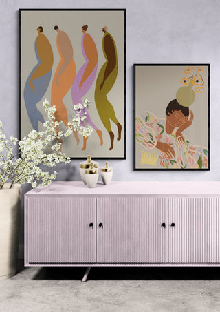 Framed Arty Guava prints above a pink sideboard with vases and white flowers, on display in a modern room.