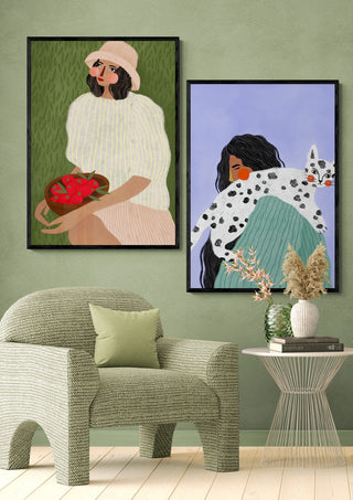 Art print of a woman with long dark hair holding a spotted cat, displayed above a modern green chair.