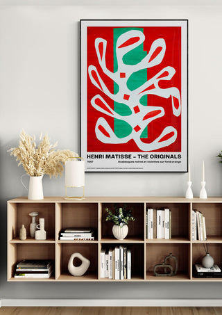 Arabesques by Henri Matisse poster with abstract white shapes on red and green, displayed above a modern shelf.