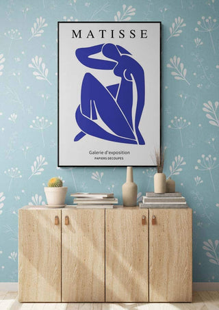 Framed Matisse Blue Nude art print hanging above a wooden cabinet in a modern, floral-themed room.