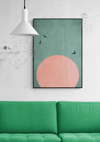 Framed "A Beautiful Day" by Boris Draschoff above a green sofa, featuring a pink sun and flying birds.