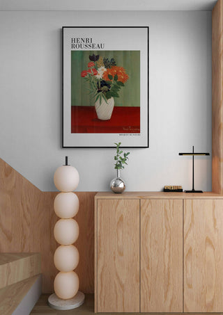 Poster of "Bouquet De Fleurs 1910" by Henri Rousseau hanging above a modern wooden cabinet in a minimalist room.