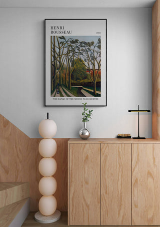 Framed "The Banks Of The Bier" by Henri Rousseau displayed above a modern wooden cabinet in a minimalist room.