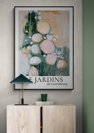 Framed abstract art print "Le Jardin Du Luxembourg 01" displayed above a light wood cabinet and green lamp.