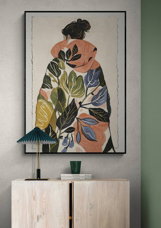 Framed artwork of a woman in a leaf-patterned coat, displayed above a modern cabinet with decor accents.